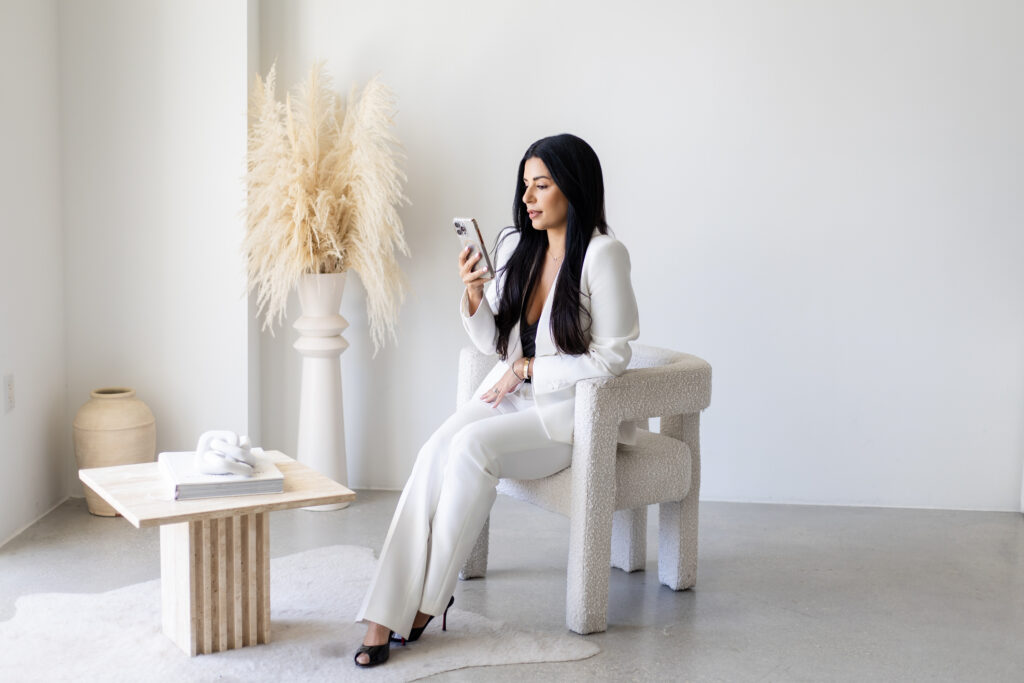 Woman in a white suit reviewing her phone while seated in a modern, minimalist room